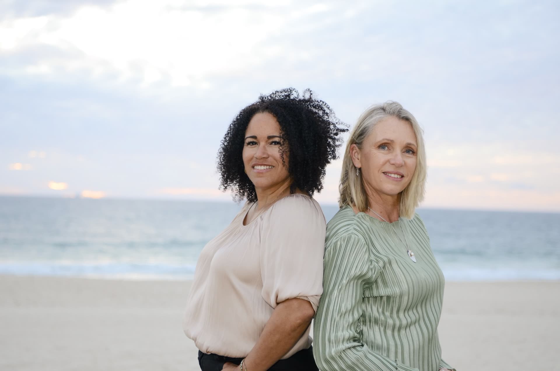 Laila and Jodie standing back to back on the beach at sunset